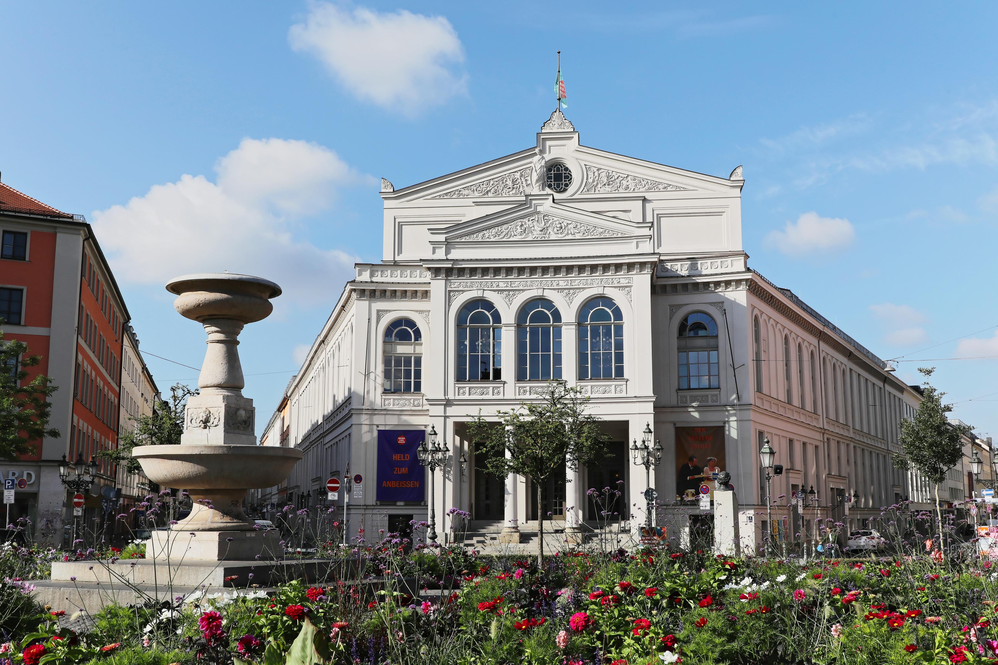 Totalen und Details vom Gebäude des Staatstheaters am Gärtnerplatz, mit Blumenrabatte und Brunnen im Vordergrund